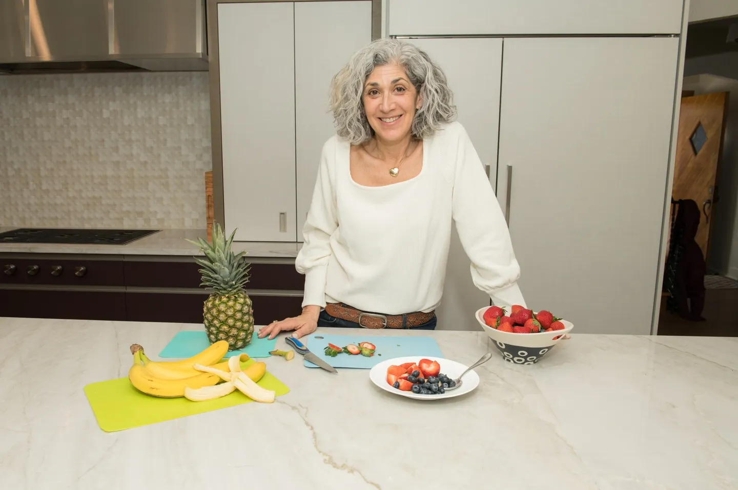 A woman standing in front of some fruit on the counter.