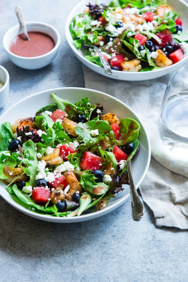 A bowl of salad with fruit and nuts.