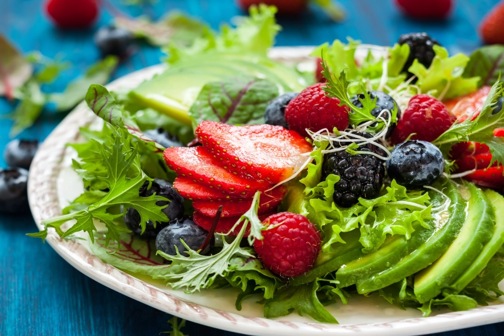 A plate of salad with strawberries and blueberries.