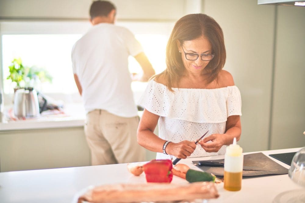 A woman in white shirt cutting vegetables on table.