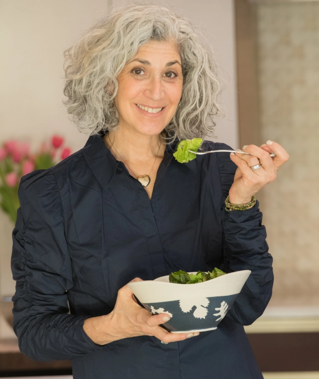 A woman with grey hair holding a bowl of salad.