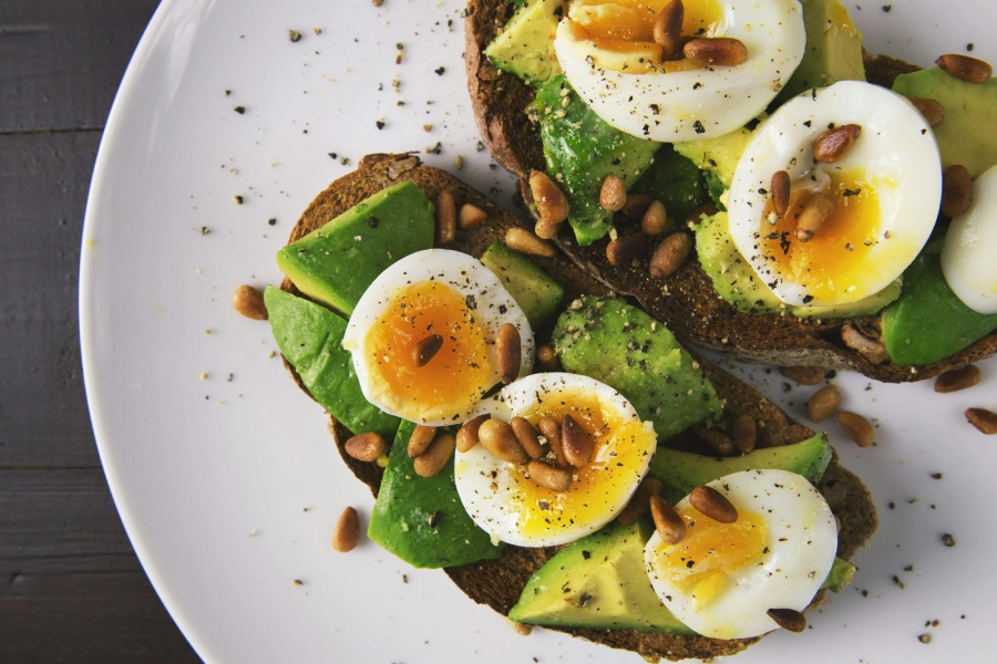 A plate of food with eggs, avocado and pine nuts.