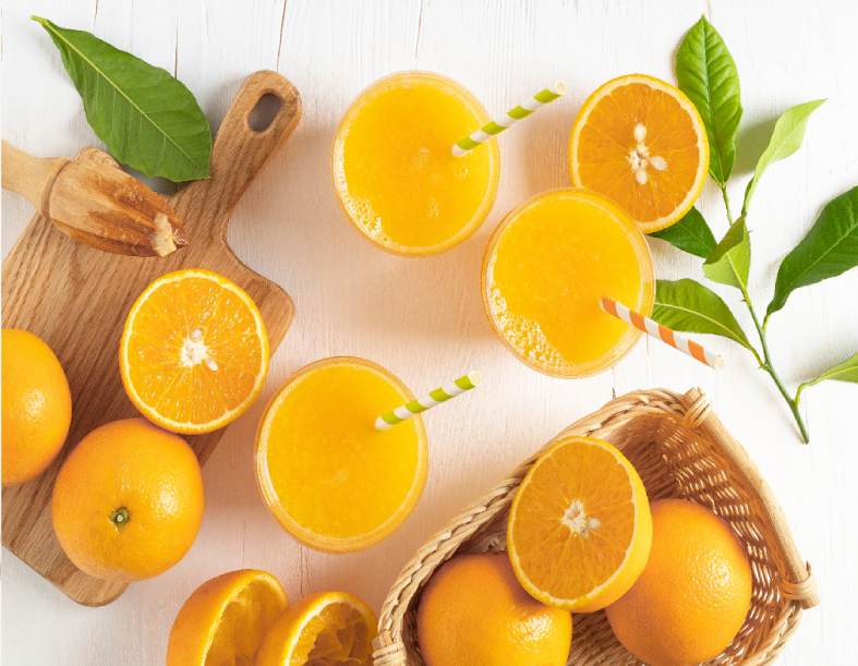 A table topped with oranges and juice next to some leaves.