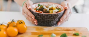 A person holding a bowl of food on top of a table.