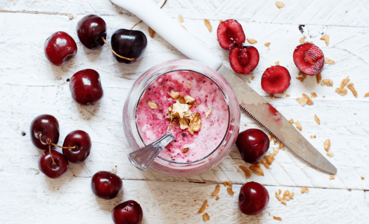 A bowl of yogurt with cherries and nuts on the side.