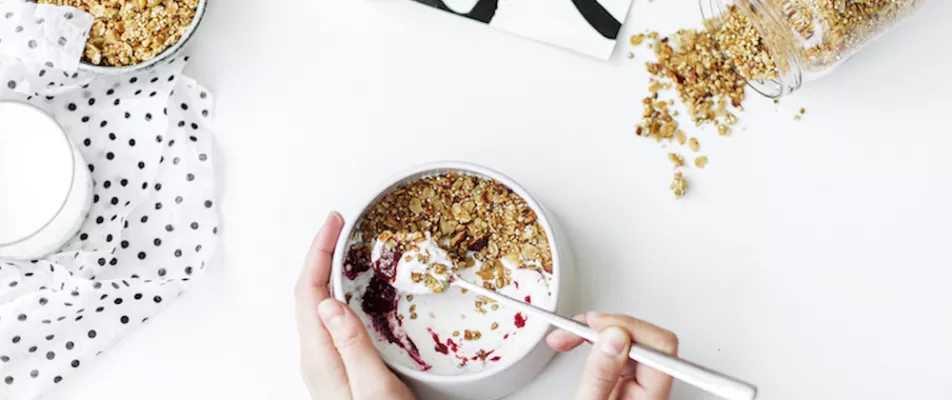 A person is eating cereal with yogurt and fruit.