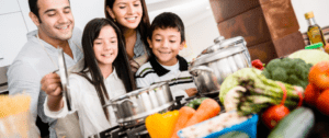 A group of people in the kitchen with pots and vegetables.