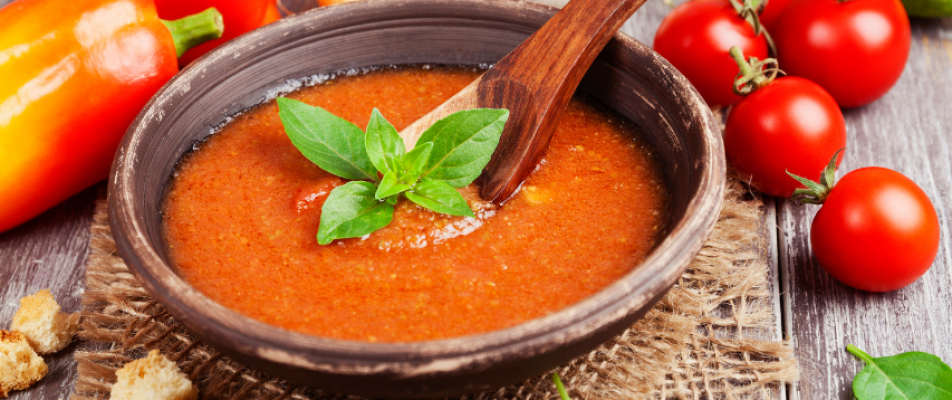 A bowl of tomato soup with basil leaves in it.