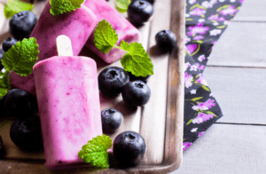 A wooden tray with blueberries and ice cream on it.