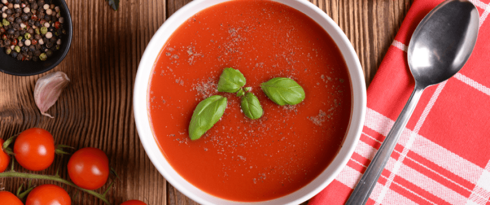 A bowl of tomato soup with basil leaves.