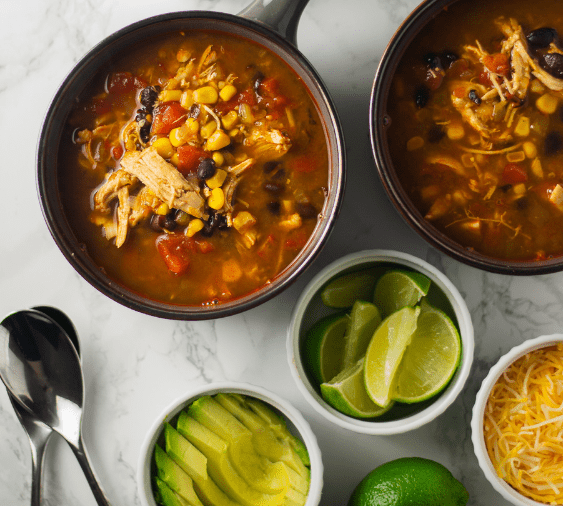 A bowl of soup with corn, avocado and lime.