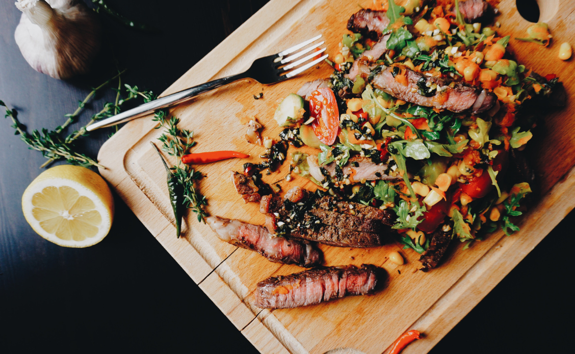 A wooden cutting board with meat and vegetables on it.