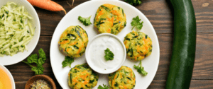 A white plate topped with baked vegetables next to a bowl of dip.