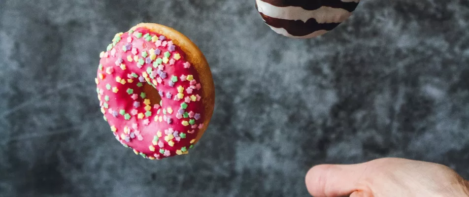 A person is reaching for the sprinkles on a doughnut.
