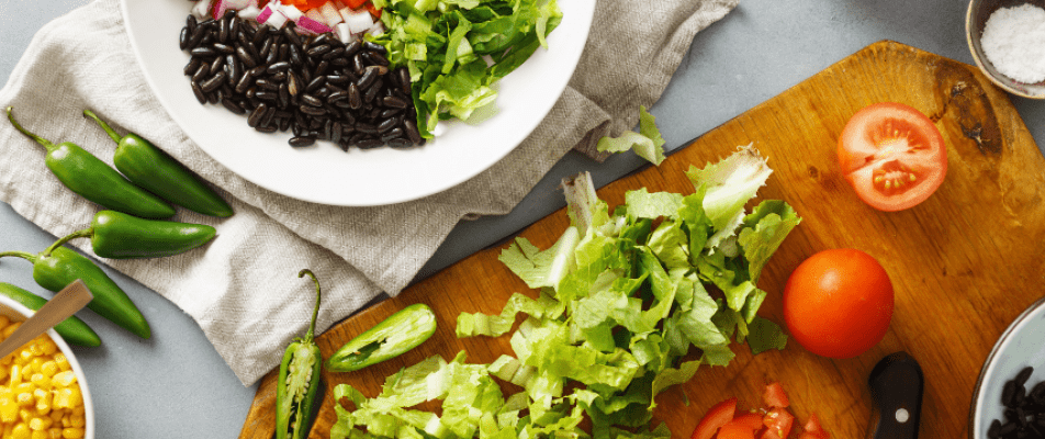 A wooden cutting board topped with lettuce next to a bowl of black beans.