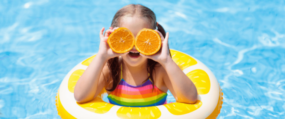 A little girl holding two oranges in front of her eyes.