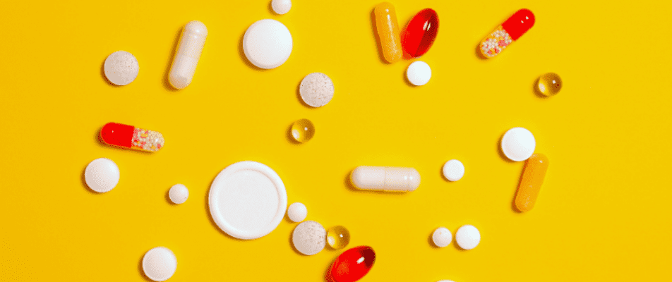 A yellow table with many different pills and capsules.