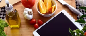 A bowl of fruit and tomatoes next to an ipad.