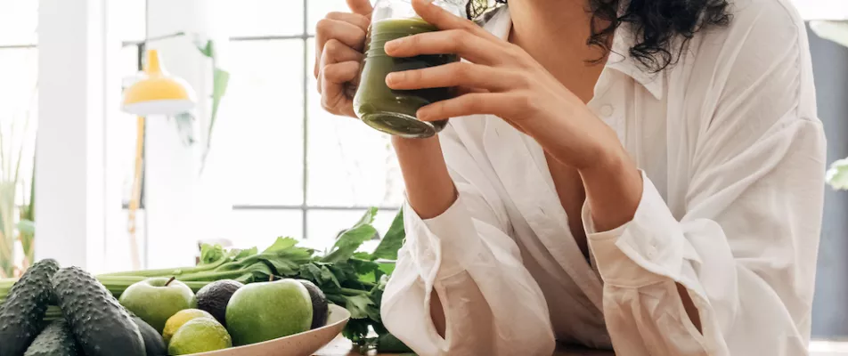 A woman is drinking from a green smoothie.