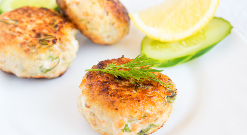 A plate of crab cakes with lemon and cucumber.