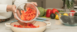 A person is putting chopped up carrots into a bowl.