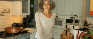 A woman standing in the kitchen wearing jeans and white shirt.