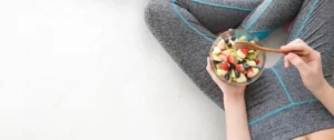 A person holding a bowl of fruit on top of a table.