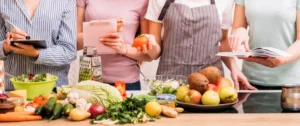 Two women standing in front of a table with fruits and vegetables.