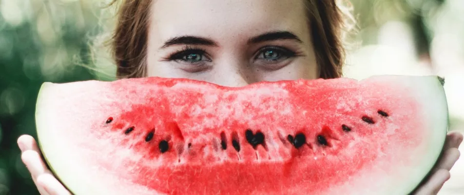 A woman with blue eyes holding up a watermelon.