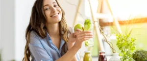 A woman holding an apple and drinking from a bottle.