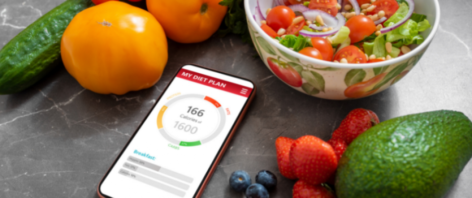 A smart phone sitting next to bowl of fruit.