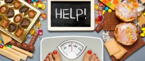 A person standing on a scale with candy and a sign that says help.